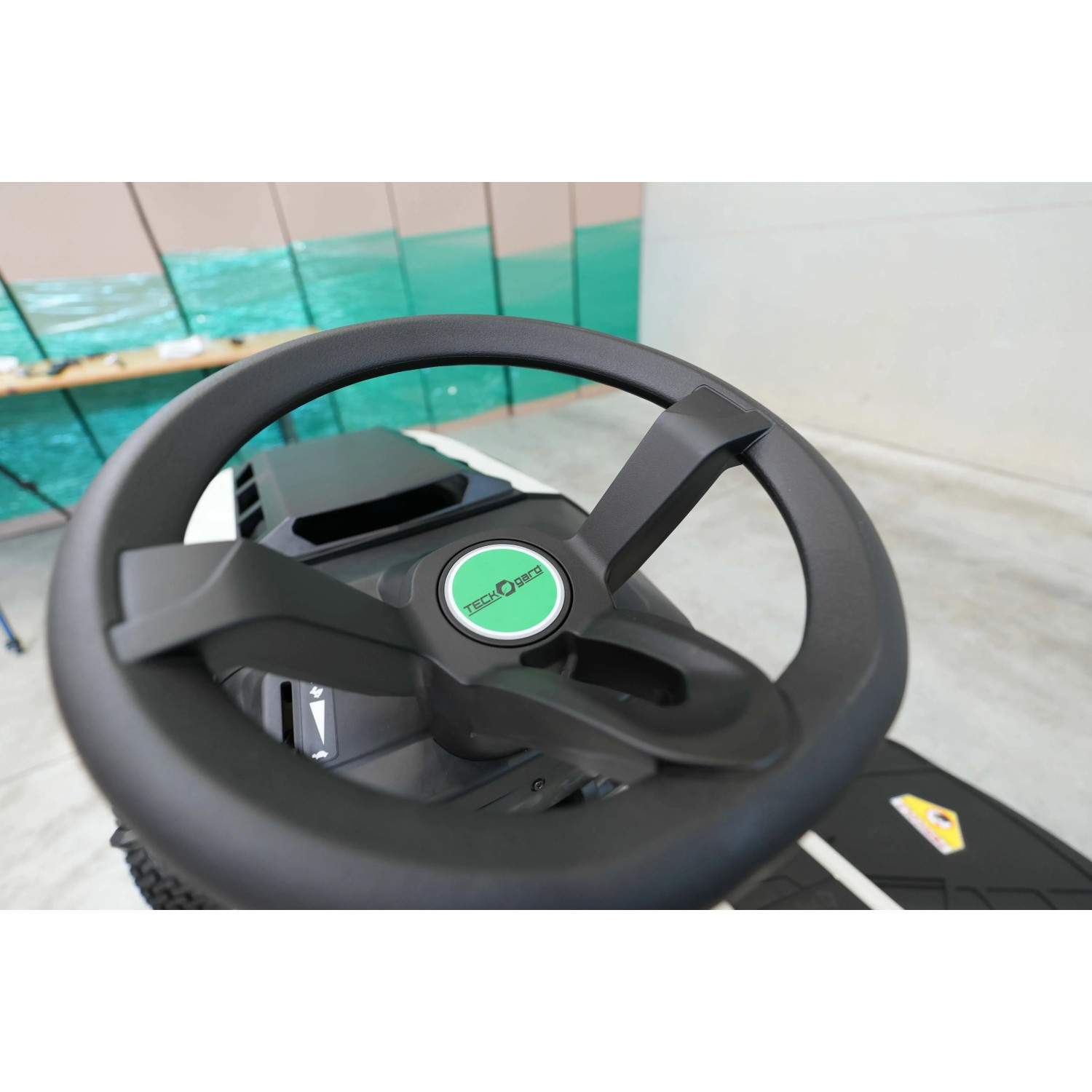 Dettaglio del volante di un trattorino tagliaerba. Volante nero con logo verde.