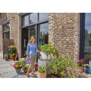 Donna che annaffia le piante con set tubo a spirale Gardena (10 m) in giardino.