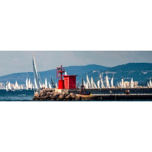 Vista panoramica di barche a vela sul mare con un faro rosso in primo piano.