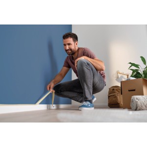 Uomo applica nastro adesivo alla parete. Nastro per mascheratura per bordi puliti.