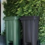 Due pattumiere t.b.t. verdi e antracite con coperchio e pedale davanti a una siepe verde.