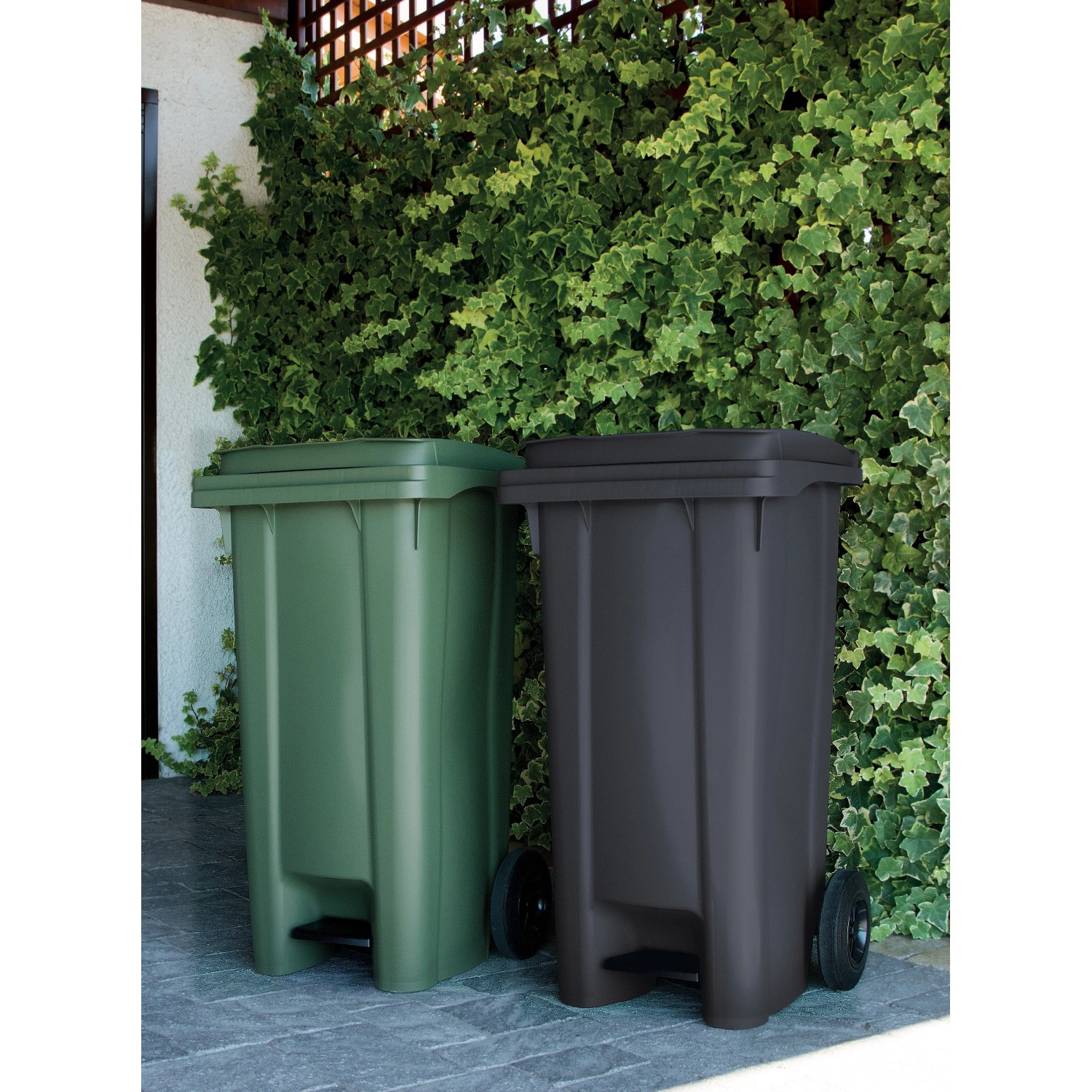 Due pattumiere t.b.t. verdi e antracite con coperchio e pedale davanti a una siepe verde.