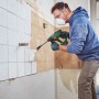 Uomo scalpella piastrelle con martello demolitore a batteria Bosch UniversalHammer 18V. Utensile verde, ristrutturazione.
