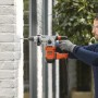 Uomo che fora un muro di mattoni bianchi con un martello perforatore Black+Decker BEHS03K.