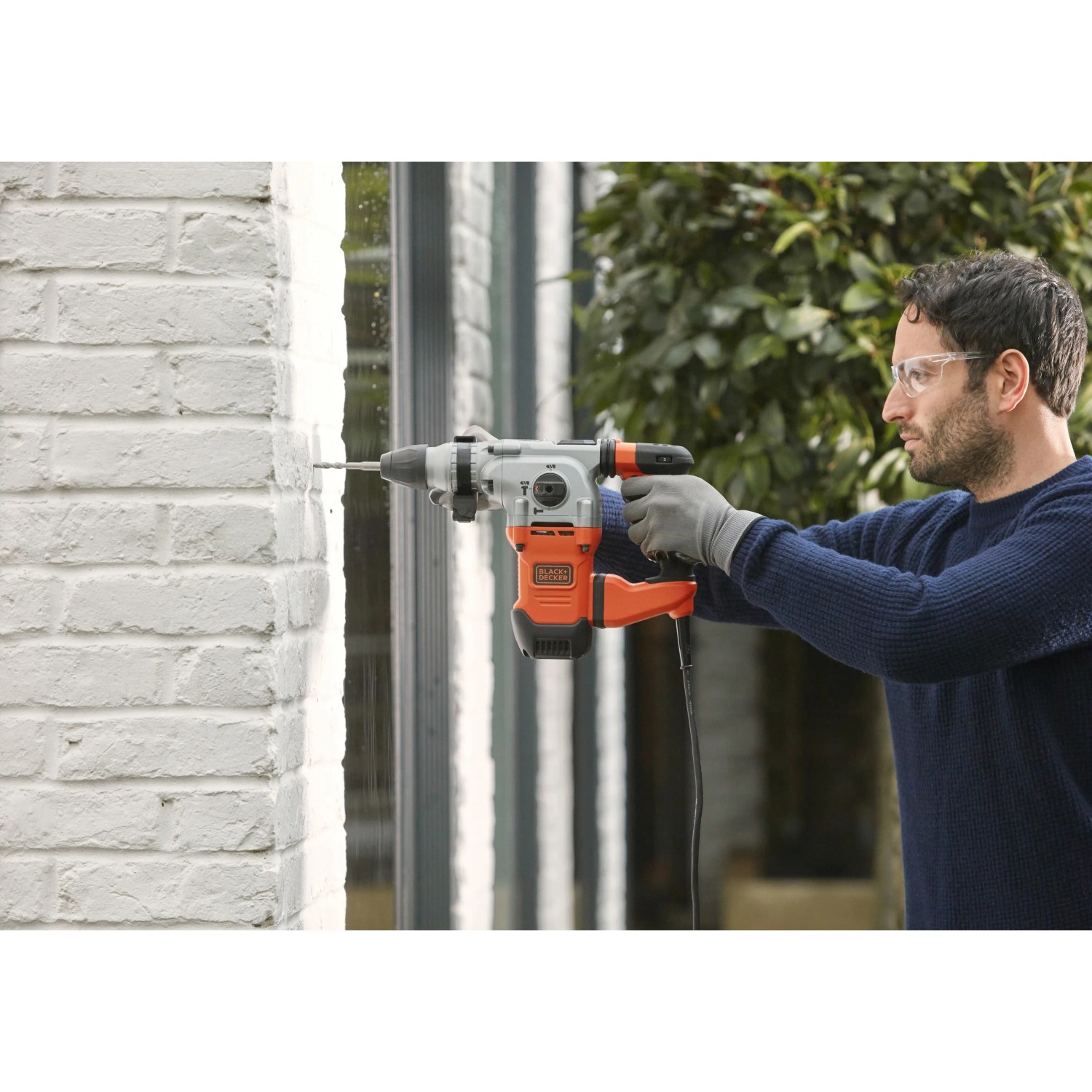 Uomo che fora un muro di mattoni bianchi con un martello perforatore Black+Decker BEHS03K.