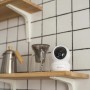 Telecamera di videosorveglianza t.b.t. bianca su mensola di legno davanti a parete di piastrelle bianche.