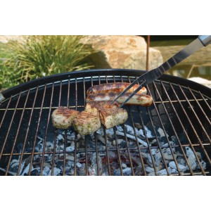 Cibo grigliato (salsicce, carne) su griglia con pinze. Accessori per barbecue.