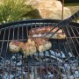 Cibo grigliato (salsicce, carne) su griglia con pinze. Accessori per barbecue.