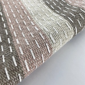 Dettaglio di un tappeto da bagno a righe con cuciture decorative bianche.