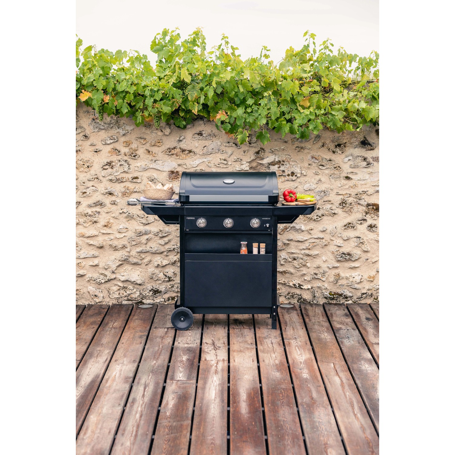 Barbecue a gas nero t.b.t. con tre bruciatori davanti a un muro di pietra con viti.