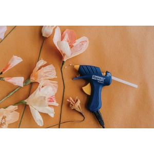 Pistola per colla blu con fiori di carta su sfondo ocra. Ideale per l'artigianato e la decorazione.