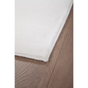 Dettaglio di un tappeto a pelo lungo bianco t.b.t. su pavimento in legno.