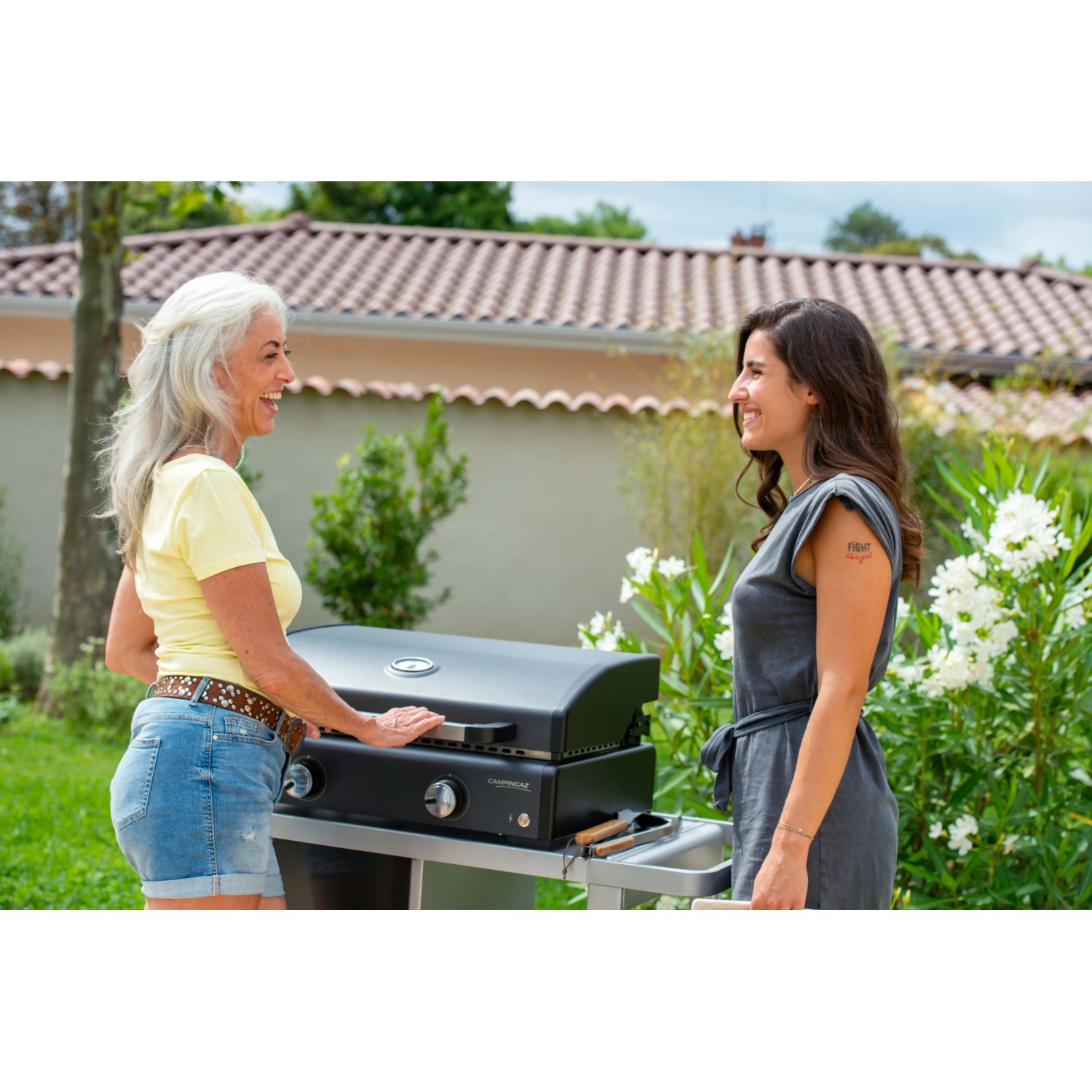 Due donne al barbecue da campeggio nero in giardino. Attrezzatura da campeggio.