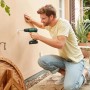 Uomo che fora un muro con un trapano avvitatore a percussione a batteria Bosch. Incl. batteria e custodia.