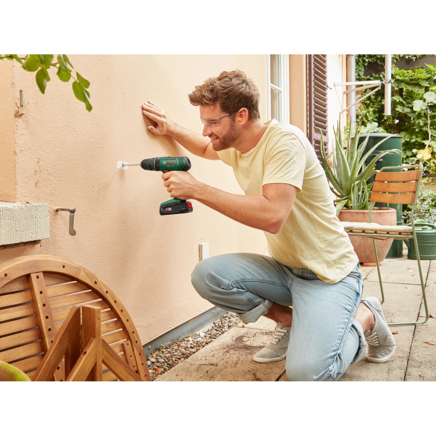 Uomo che fora un muro con un trapano avvitatore a percussione a batteria Bosch. Incl. batteria e custodia.