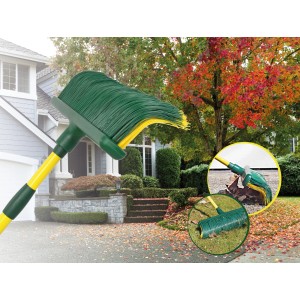 Rastrello per foglie verde con manico giallo davanti a casa e giardino in autunno.