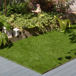 Prato sintetico verde t.b.t. come pavimentazione in giardino, circondato da piante.