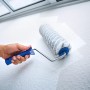 Rullo per pittura LUX 25cm in uso: rullo con manico blu che dipinge una parete bianca.