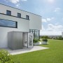 Armadio da esterno Biohort Large, grigio quarzo metallizzato, con porta aperta e attrezzi da giardino davanti a una casa moderna.