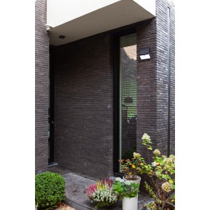 Lampada da parete solare a LED Lutec Tuda nera con sensore di movimento su muro di casa scuro.