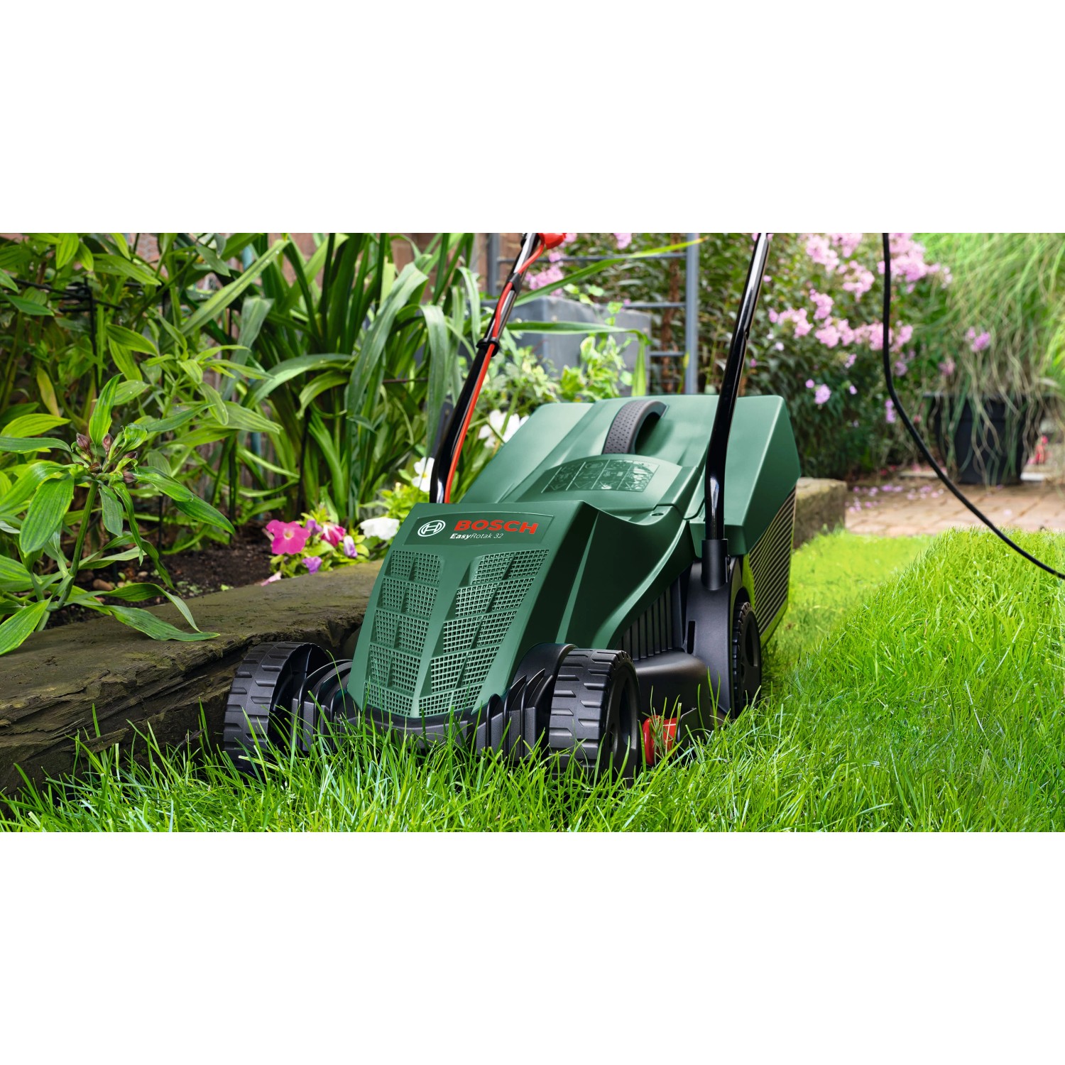Rasaerba elettrico Bosch Easy Rotak 32-215 verde taglia l'erba lungo il bordo di un'aiuola in giardino.