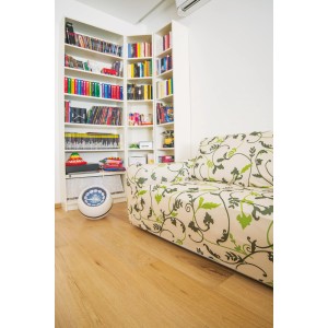 Soggiorno con libreria e divano con rivestimento floreale. Cuscini e copricuscini sullo sfondo.