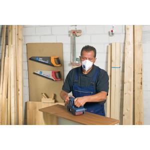Uomo che leviga il legno indossando una maschera LUX FFP2 con valvola. Protezione respiratoria per il fai da te.