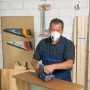 Uomo che leviga il legno indossando una maschera LUX FFP2 con valvola. Protezione respiratoria per il fai da te.