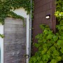 Lampada da parete solare a LED Lutec Try nero opaco su muro di casa con piante.