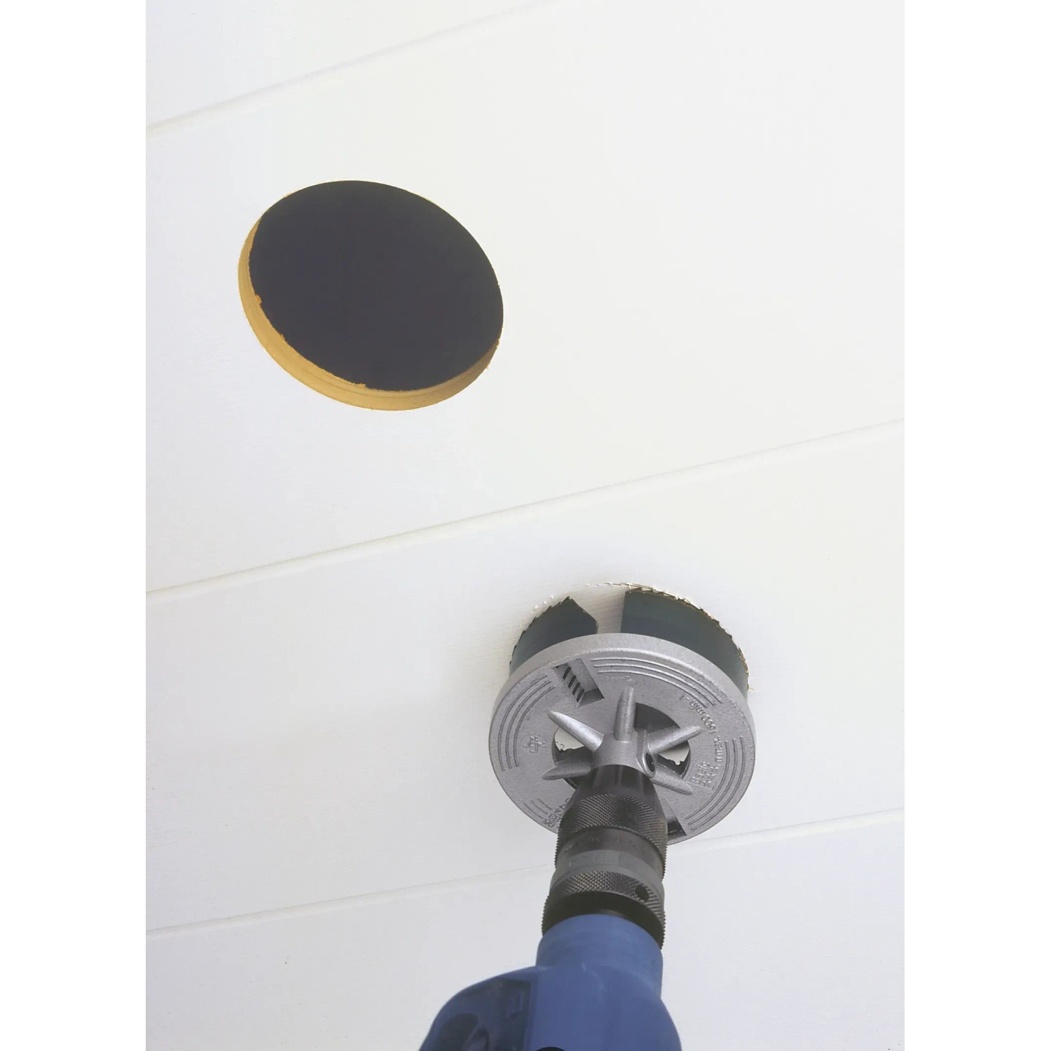 Set di seghe a tazza LUX in uso: Foratura di un foro in un soffitto bianco con un trapano.