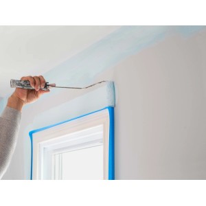 Imbianchino che dipinge la parete con rullo e nastro adesivo.