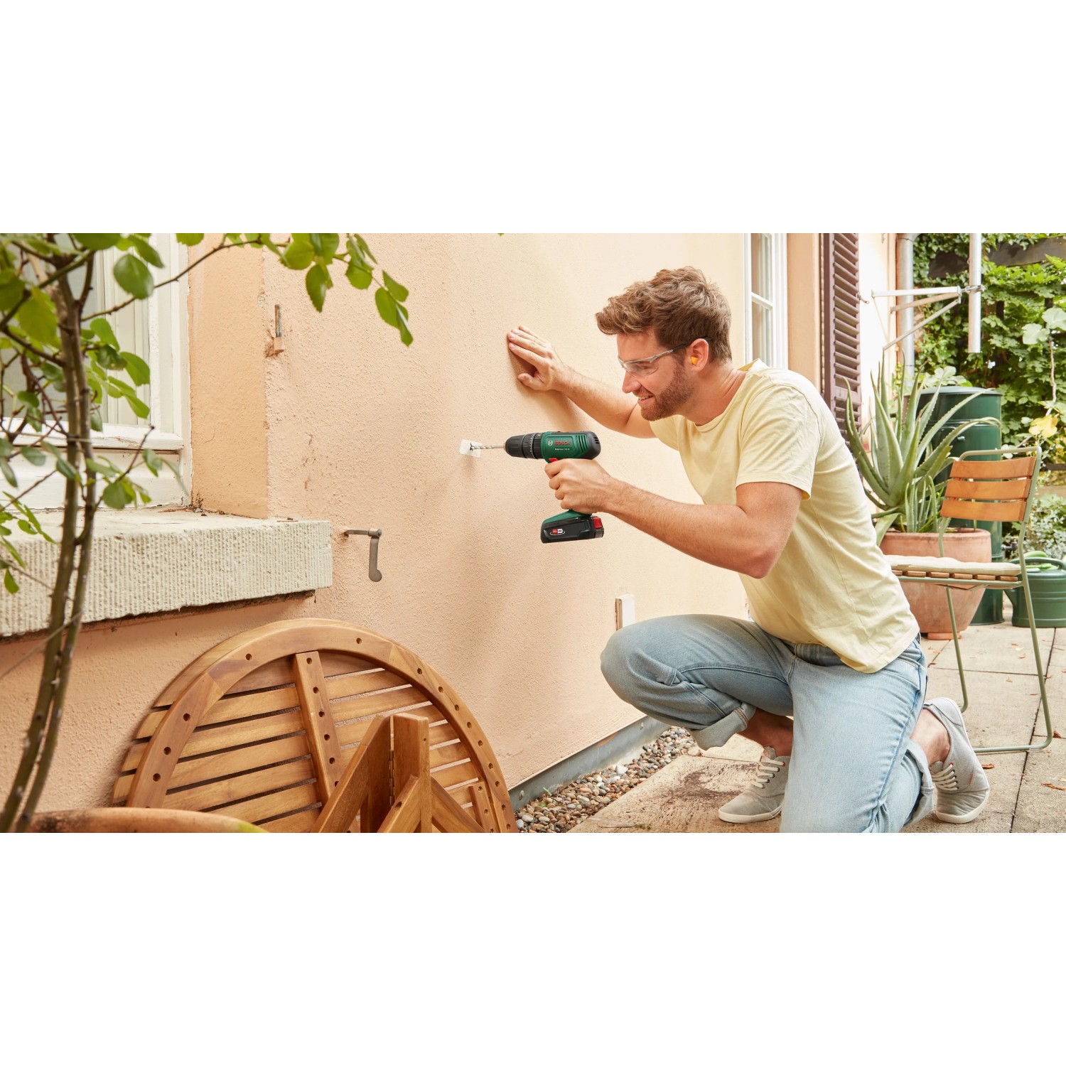 Uomo che fora un muro con trapano avvitatore a percussione a batteria Bosch 18V. Include batteria e custodia.