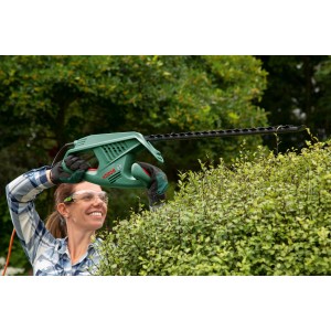 Donna taglia la siepe con il tagliasiepi elettrico Bosch EasyHedgeCut 45. Il dispositivo è verde e nero.
