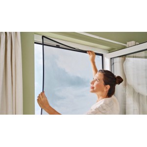 Donna che installa la zanzariera a clip tesa® Insect Stop (antracite) sulla finestra. Protezione insetti per finestre.