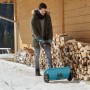 Uomo che usa lo spargitore Gardena L in inverno per spargere sale su una superficie innevata.
