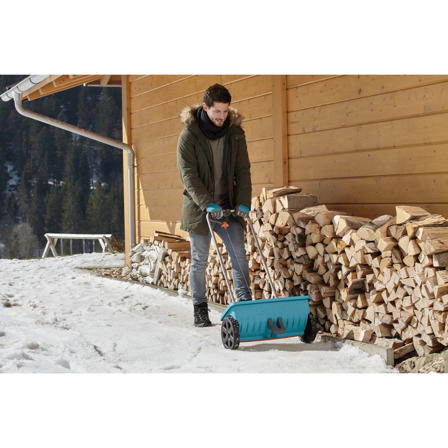 Uomo che usa lo spargitore Gardena L in inverno per spargere sale su una superficie innevata.