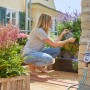 Computer per irrigazione Gardena Flex su rubinetto con donna che fa giardinaggio sul balcone.