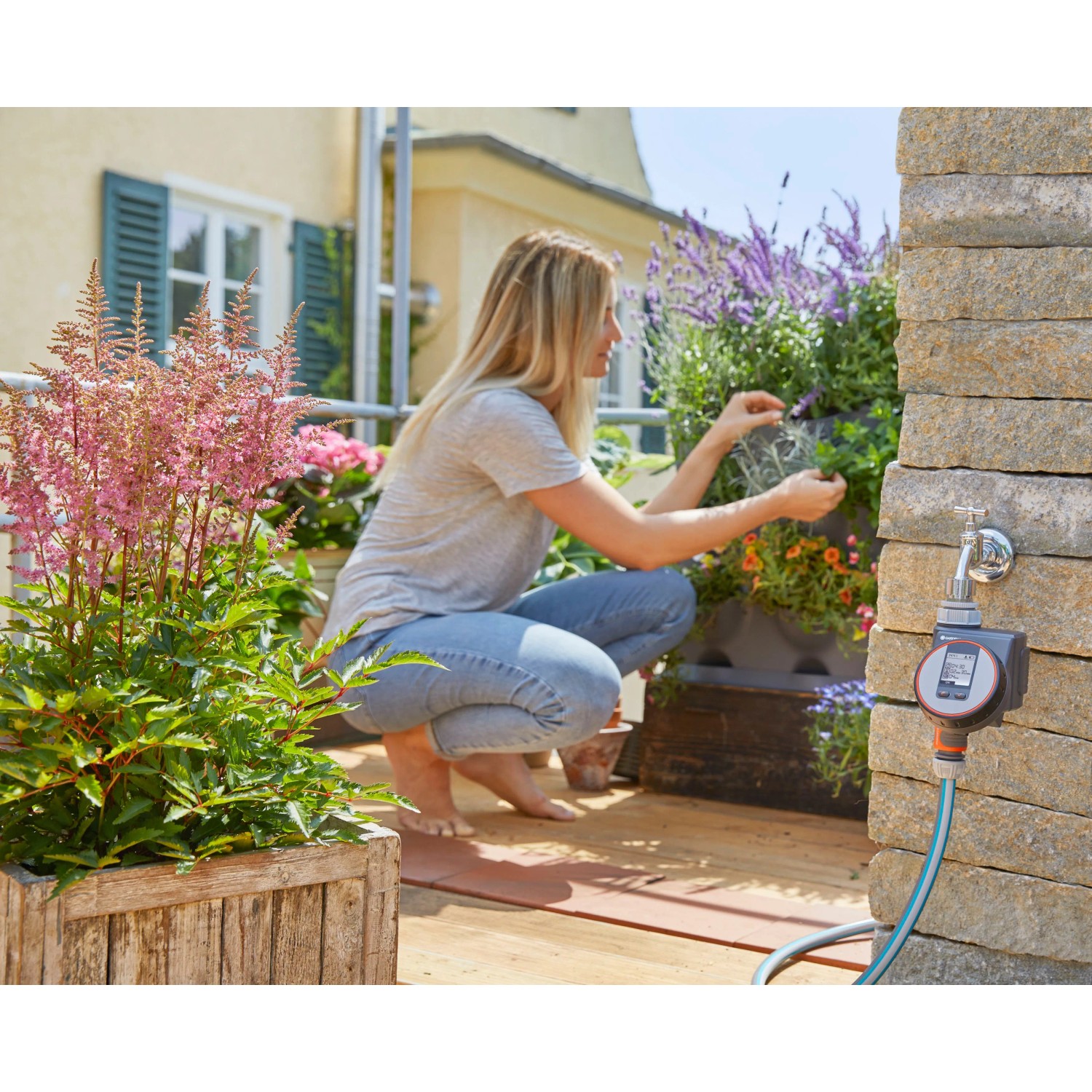 Computer per irrigazione Gardena Flex su rubinetto con donna che fa giardinaggio sul balcone.