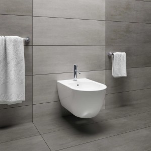 Bidet bianco sospeso con rubinetto e asciugamani in bagno moderno.