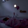 Bambina a letto sotto lampade da parete a forma di palloncino. Lampada LED per cameretta.