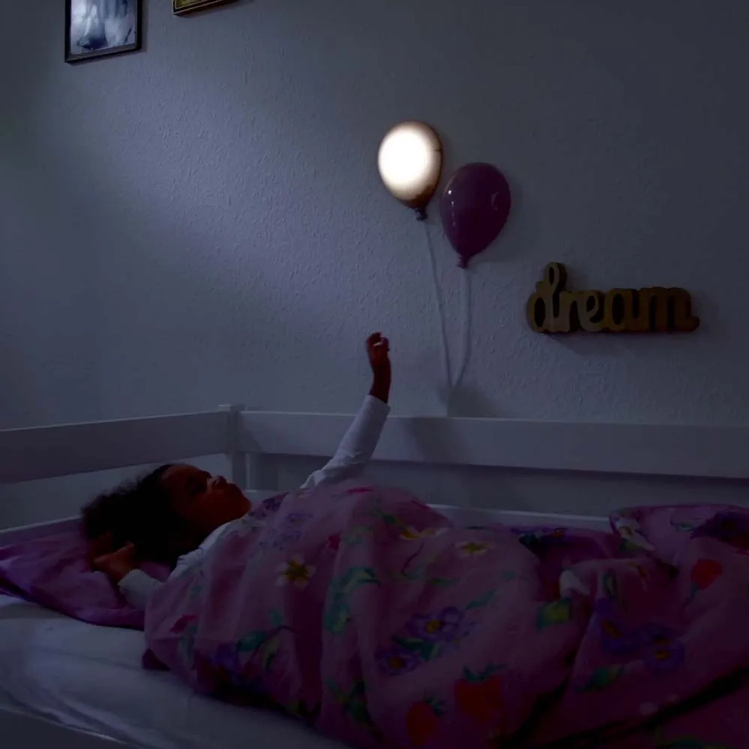 Bambina a letto sotto lampade da parete a forma di palloncino. Lampada LED per cameretta.
