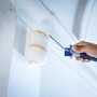 Rullo per pittura LUX 15 cm in uso: mano che dipinge parete bianca con rullo.