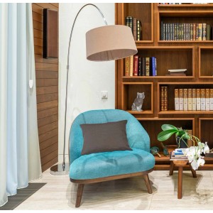 Poltrona turchese con cuscino marrone davanti a libreria e lampada da terra.