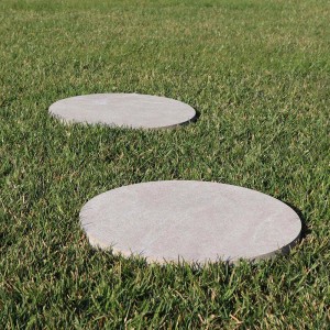 Due lastre di camminamento rotonde t.b.t. in pietra naturale nell'erba verde. Design del percorso del giardino.