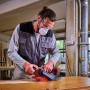 Levigatrice a nastro a batteria Einhell TP-BS 18/457 Li BL Solo mentre leviga il legno.