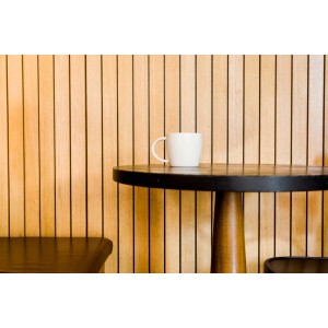 Tazza bianca su tavolo rotondo davanti a parete con pannelli di legno. Perline.