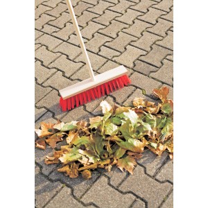 Scopa stradale LUX 40 cm con manico e setole rosse, accanto a un mucchio di foglie su pavimentazione.
