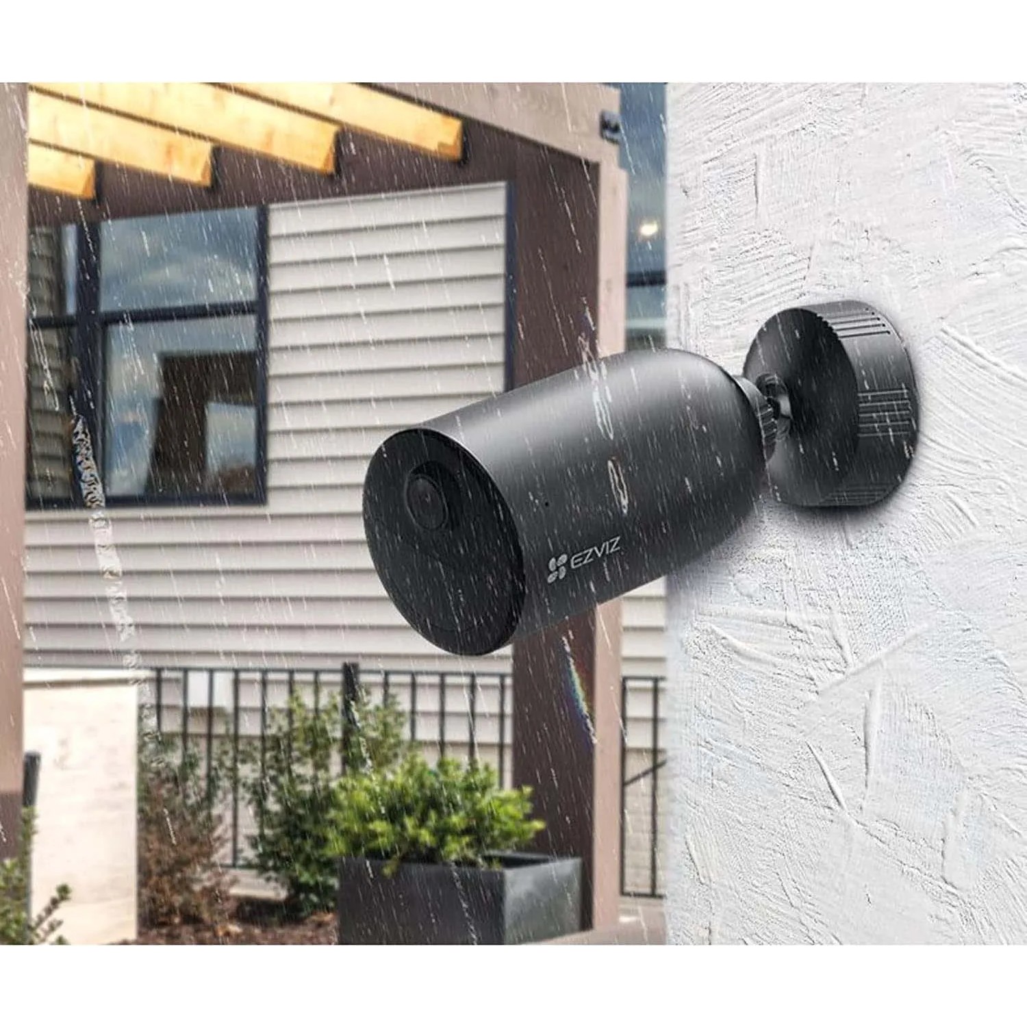 Telecamera di sorveglianza da esterno a batteria Ezviz EB3 nera montata su una parete di casa sotto la pioggia.