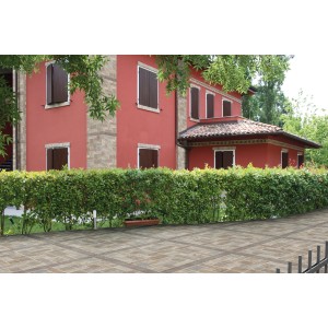 Piastrelle da rivestimento posate di fronte a una casa con facciata rossa e siepe verde.