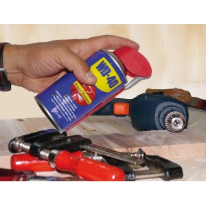 Bomboletta spray multiuso WD-40 in mano, trapano sullo sfondo.